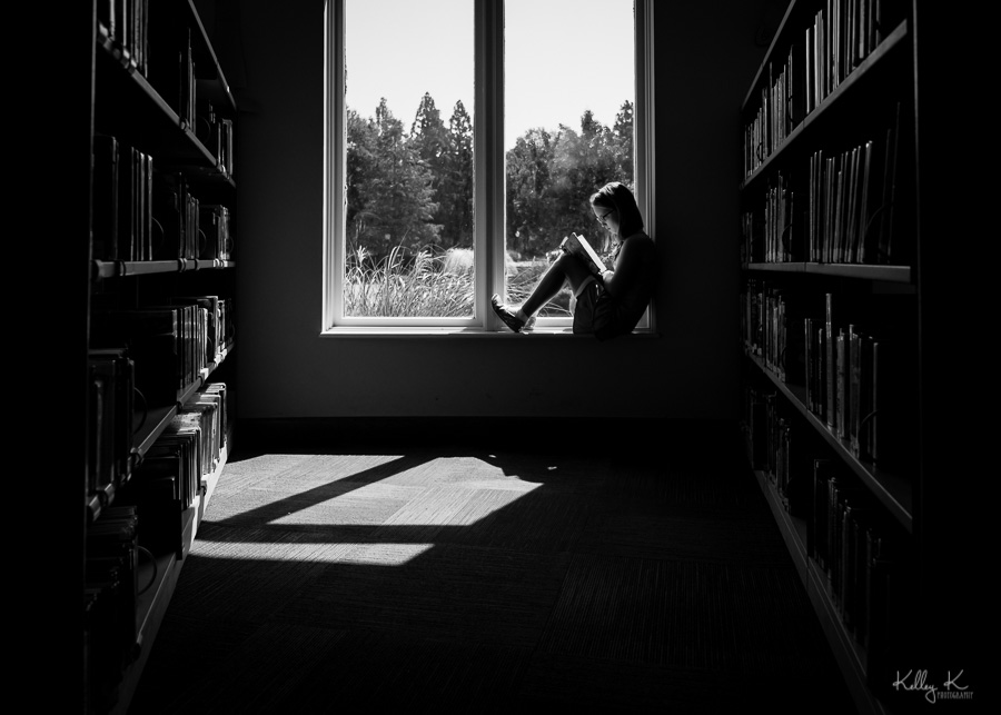 Black and white silhouette of girl reading in a library window